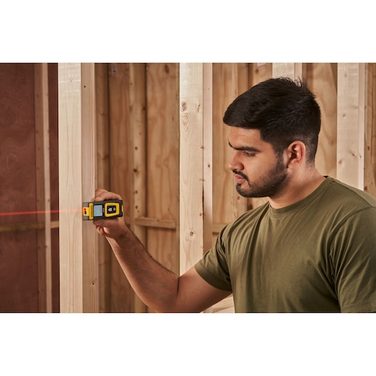 STANLEY STHT77100-0 laser distance measurer in use on wooden framing, handheld with visible red laser beam.