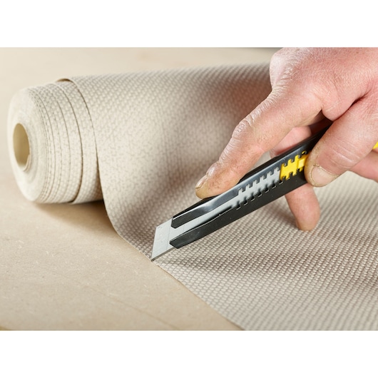 STANLEY STHT9-11301 utility knife cutting textured wallpaper in close-up photography.