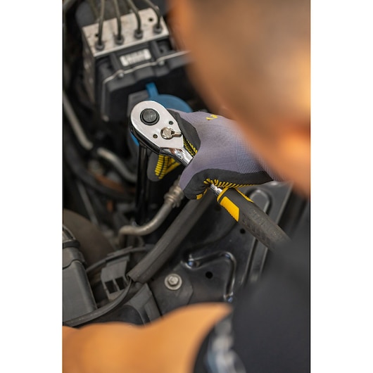 STANLEY STMT86007-0 ratchet wrench used on engine, close-up of gloved hand during automotive repair.
