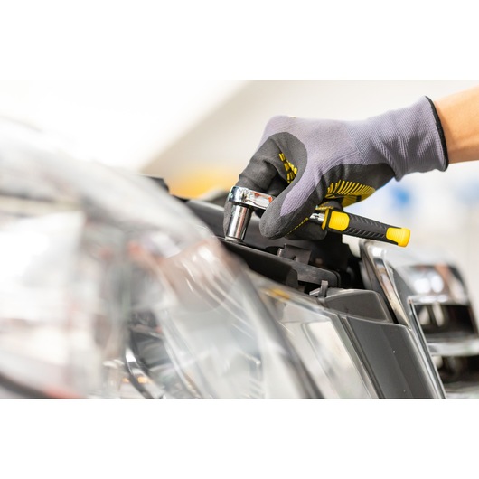 STANLEY STMT86103-0 ratchet wrench used on car headlight, close-up, gloved hand, automotive photography.