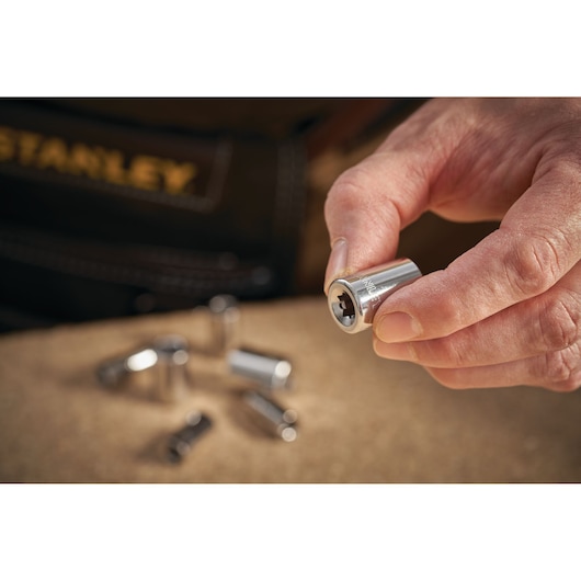 STANLEY STMT86104-0 chrome socket set shown in hand, close-up photography with several sockets on work surface.