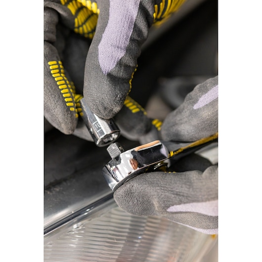 STANLEY STMT86104-0 socket wrench held by gloved hands, close-up angle, automotive setting.