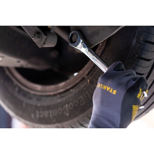 Stanley STMT89912-0 ratcheting wrench used on a car wheel, hand in Stanley glove visible.