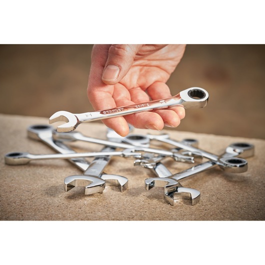 STANLEY STMT89918-0 ratcheting combination wrench set, one wrench held in hand, others on wooden surface.