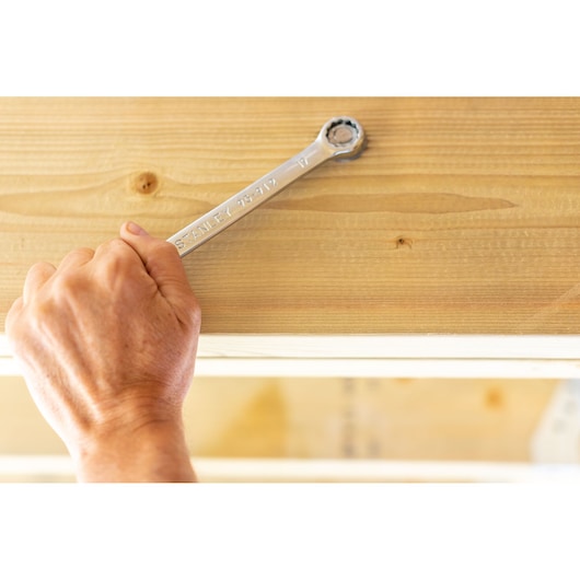 Photo of STANLEY STMT95790-0 ratcheting wrench in use against wooden beam, close-up of hand and tool.