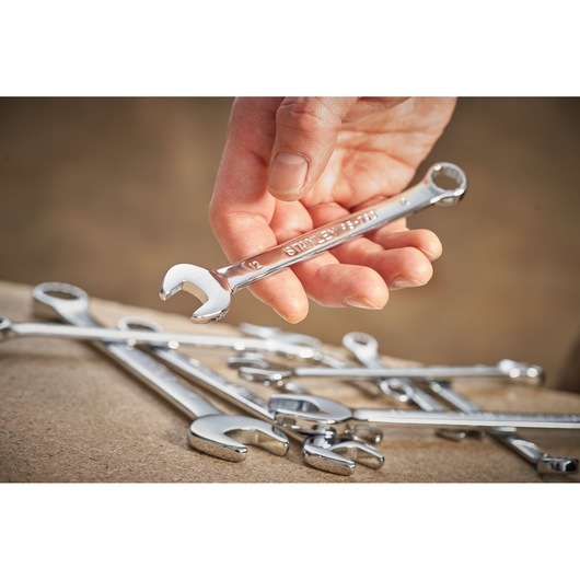 Photo of a hand holding a STANLEY STMT95791-0 combination spanner above several chrome wrenches on a work surface.