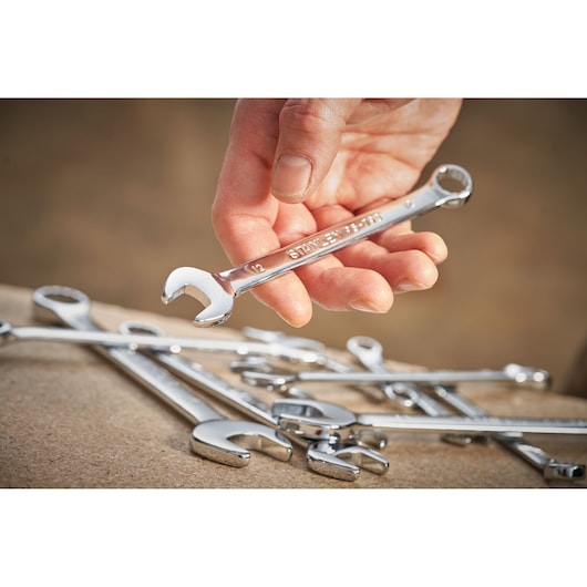 STANLEY STMT95910-0 combination wrench held in hand above several chrome wrenches on a workbench, close-up.