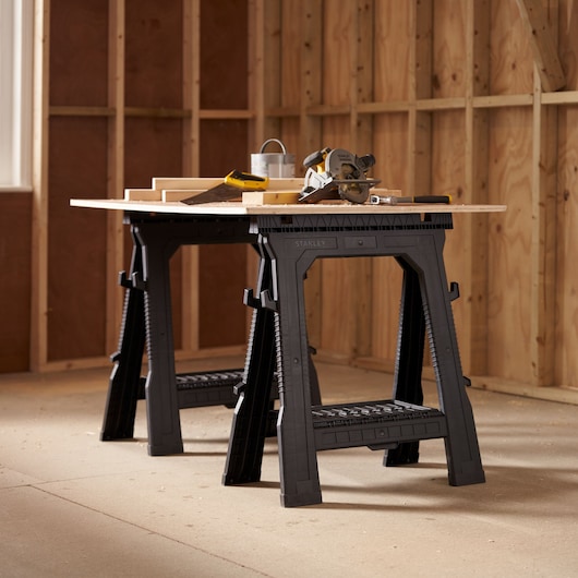 STANLEY STST1-70713 black plastic sawhorses, workshop angle, used as a workbench with tools on top.