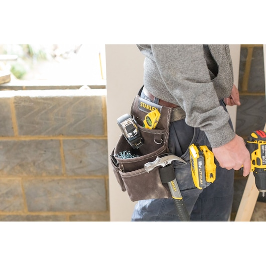 Photo of STANLEY STST1-80116 tool belt loaded with tools, worn by person in work clothes at construction site.
