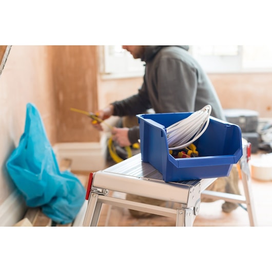 STANLEY STST82743-1 blue storage bin with cables and tools on a step ladder in a workspace.