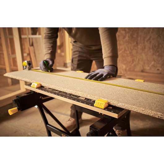 STANLEY STST83400-1 workbench with clamps holding a wood board, person measuring with tape measure.