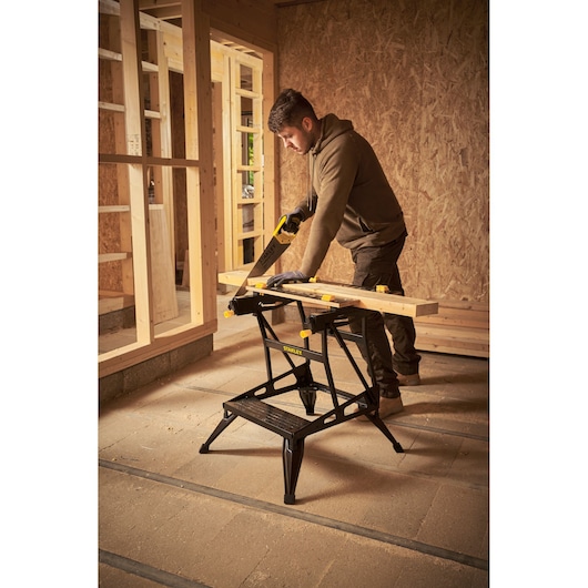 STANLEY STST83400-1 workbench in use, supporting wood for sawing in a construction setting.