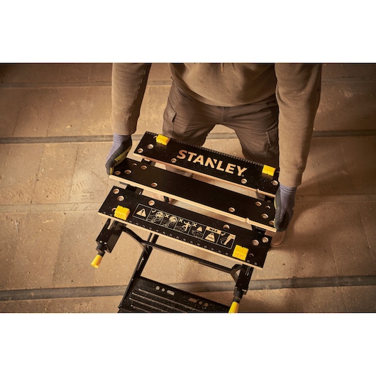 Photo of STANLEY STST83400-1 workbench with black surface, yellow clamps, and safety markings, viewed from above.