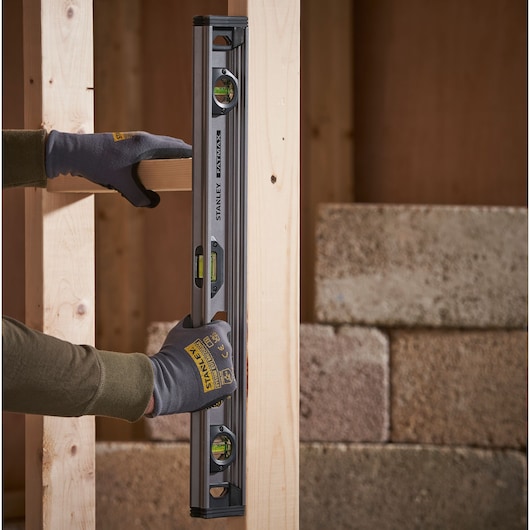 Photo of STANLEY XTHT1-42131 spirit level held vertically on wooden frame, with gloved hands.